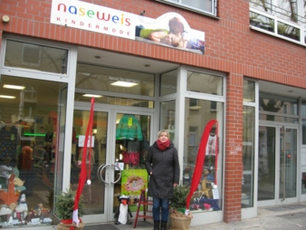 Doris Petzold vor ihrem Laden „Naseweis Kindermode“, in dem eine Präsentationswand zeigt, wie Fashion für Kids angezogen aussieht.